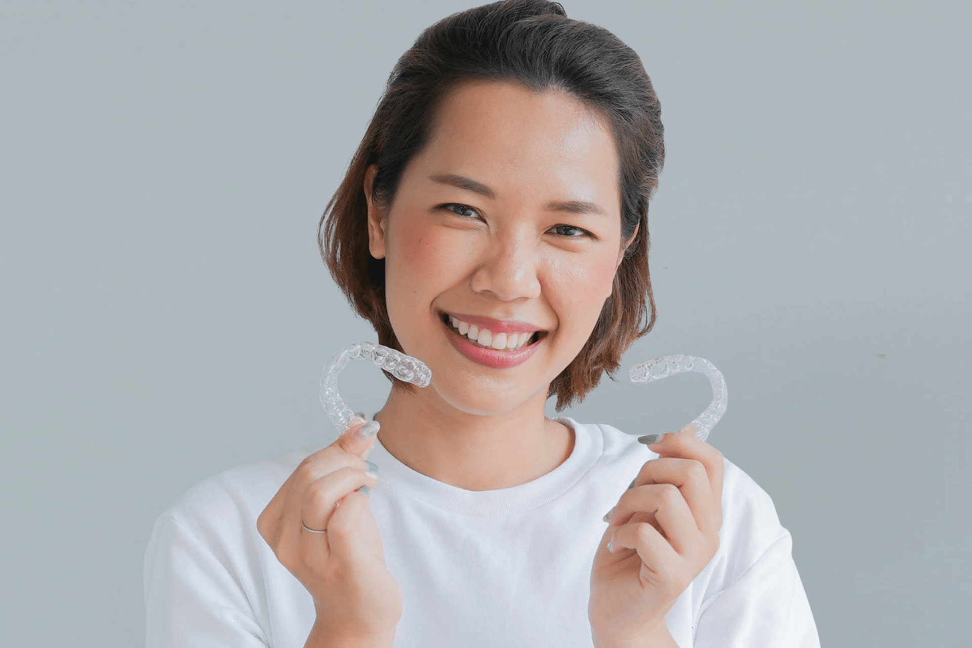 Smiling woman holding up a pair of clear dental aligners