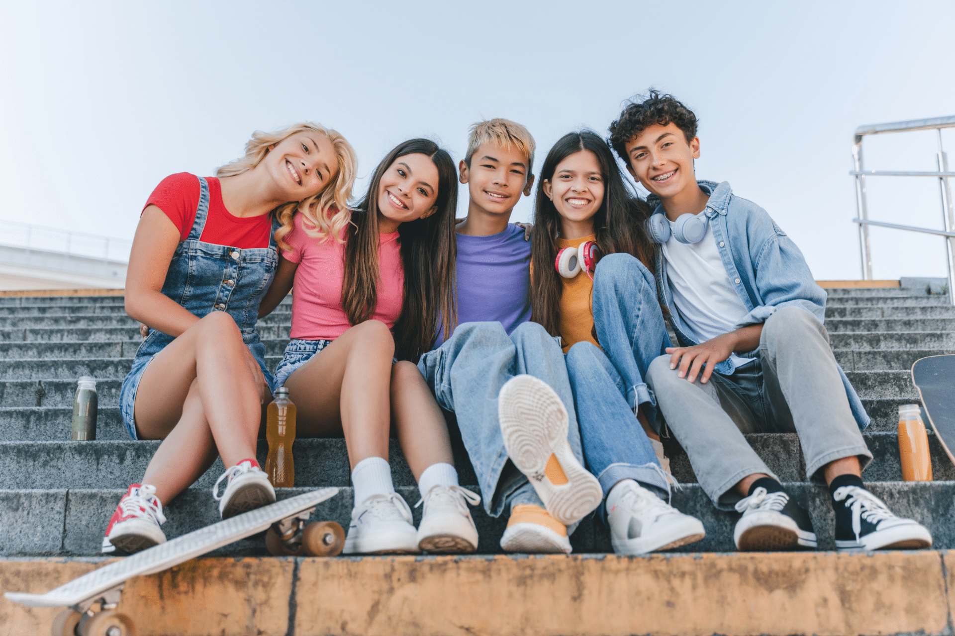 Five smiling teenagers, including one wearing braces, sitting together on outdoor steps.