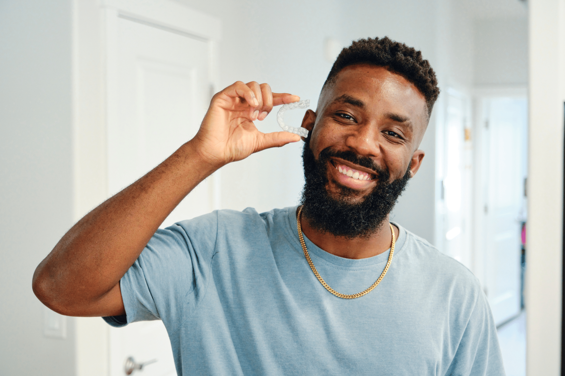 Smiling man holding a clear dental aligner beside his face.